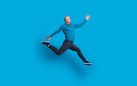 Caucasian man with blonde hair and beard dressed in blue is jumping and imitate running on a blue...