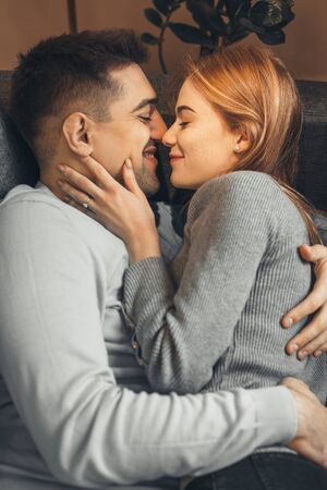 Handsome caucasian boy holding his girlfriend with red hair and freckles while lying on the sofa