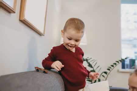 Childish caucasian boy with blonde hair is playing joyfully with his father sitting on the sofa