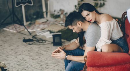 Caucasian boy with long beard is thinking about something while his wife with black hair is embracing himの写真素材