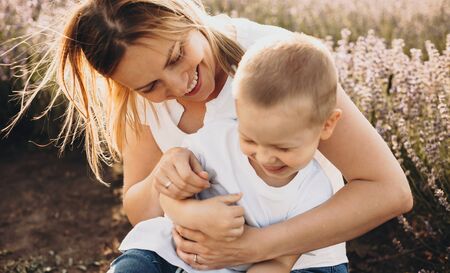 Caucasian blonde mother holding her son while having joy with him in a lavender fieldの写真素材