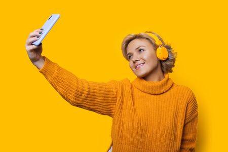 Caucasian blonde woman making a portrait of herself while listening to music on a yellow backgroundの写真素材
