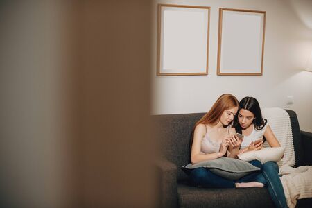 Caucasian ginger girl with freckles is showing something to her brunette friend pointing to her...