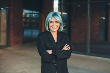 Charming caucasian businesswoman with blue hair is posing with crossed hands while looking at cameraの写真素材