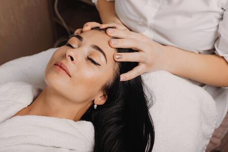 Caucasian masseur having a spa procedure of head massage with brunette charming ladyの写真素材