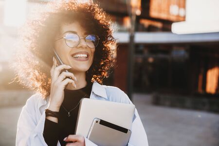 Curly haired caucasian woman posing with some modern gadgets during a phone discussionの写真素材