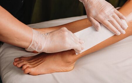 Caucasian spa worker is having a waxing session on legs with his client lying on the couchの写真素材