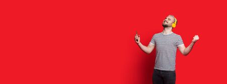 Caucasian man with beard and blonde hair is gesturing a winning while listening to music on a red...