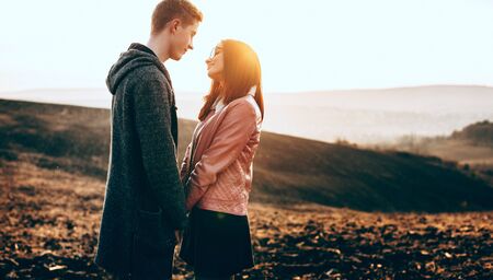 Caucasian charming couple sitting face to face and embracing during a sunny evening in a field