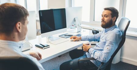 Handsome caucasian man drinking a coffee is having a dialogue with his workmate at the office.