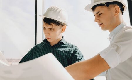 Close up photo of two caucasian men with helmet planning a building on a big paperの写真素材