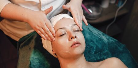Facial massage procedure done in a spa center to young caucasian woman lying with closed eyesの写真素材