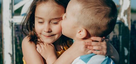 Close up portrait of a caucasian blonde boy and his sister kissing her and embracing against the...
