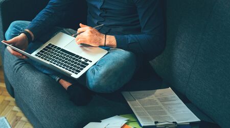Close up photo of a businessman sitting on the sofa and working with computer and documentsの写真素材