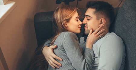 Upper view of caucasian man lying on the sofa and embracing his red haired woman with freckles