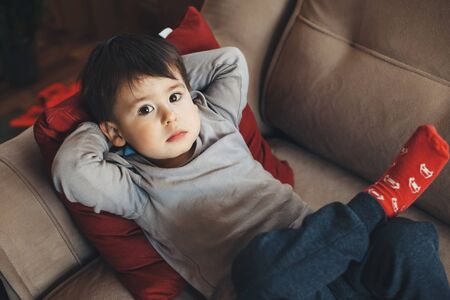 Upper view portrait of a caucasian boy resting in the sofa and looking up to camera during the...