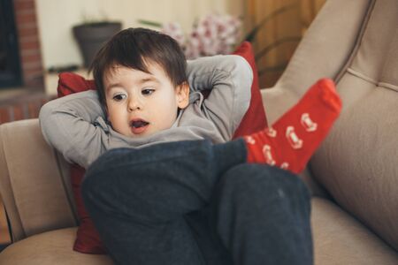 Sleepy caucasian boy with red socks posing on a sofa lying ready for a nap