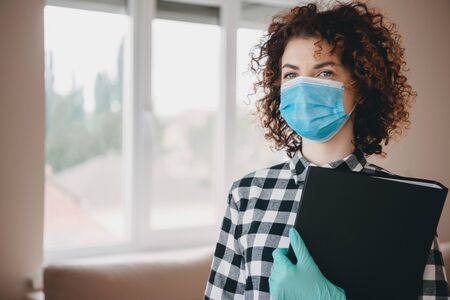 Charming caucasian doctor with curly hair holding some documents and wearing n95 face mask with glovesの写真素材