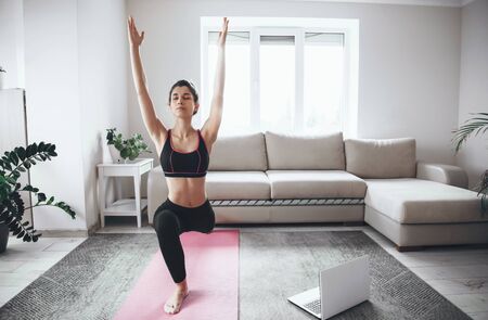 Lovely woman stretching her muscles before yoga lesson at home during the quarantine with a laptopの写真素材