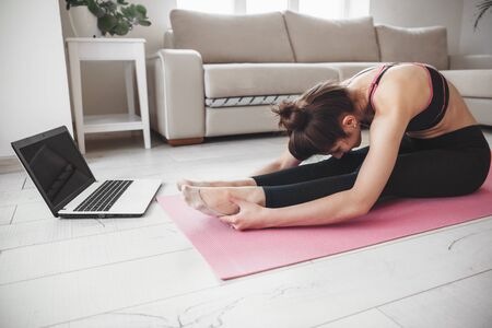Side view photo of a caucasian lady doing yoga on the floor and using a laptop while stretchingの写真素材