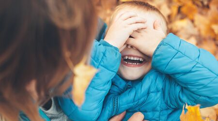 Caucasian boy and his mother playing on the ground with autumn leaves smiling with opened mouthの写真素材