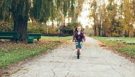 Lovely small girl on bike walking in the park alone in an autumn dayの写真素材