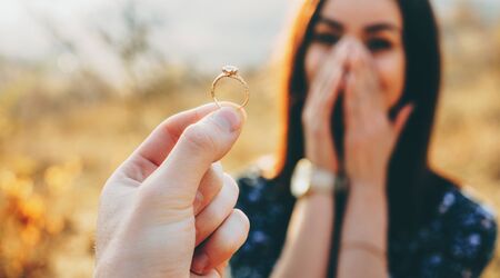 Close up photo of a wedding ring with diamond shown to the girl while she is amazed and covers her face with palmsの写真素材