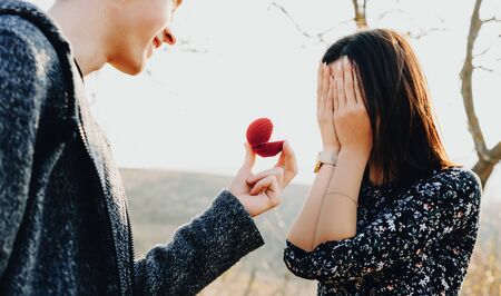 Surprised caucasian girl asked to get married by her lover in a field is covering her face with palms in front of the wedding ringの写真素材