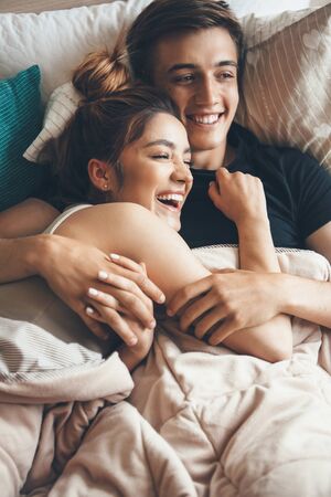 Close view photo of a happy couple lying in bed and embracing early morningの写真素材