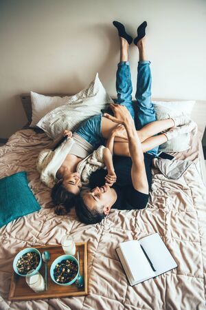 Charming couple lying in bed before eating cereals with milk near an opened bookの写真素材