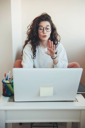 Young caucasian girl with curly hair and eyeglasses is having online lessons at the university...