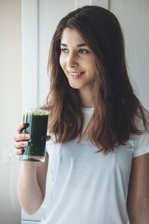 Caucasian woman with black hair drinking a glass of fresh vegetable juiceの写真素材