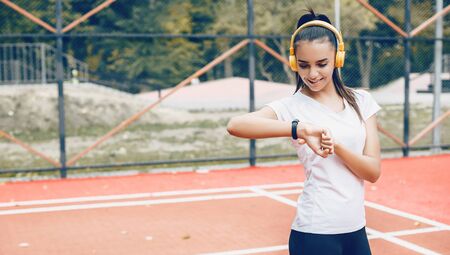Brunette caucasian girl fixing the time on her smart watches after doing morning exercises using headphonesの写真素材