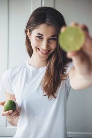 Brunette caucasian woman is smiling and showing a sliced lime to camera