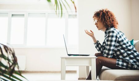 Lovely caucasian woman with curly hair and glasses explaining something at the laptop having online...