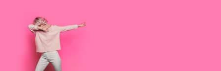 Caucasian blonde woman dabbing on a pink studio wall with empty spaceの写真素材