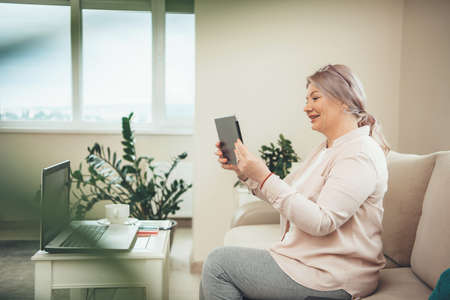 Senior blonde caucasian businesswoman with eyeglasses having a video conference on tablet while...