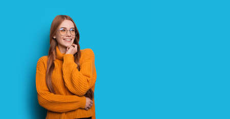Charming red haired lady with freckles and eyeglasses wearing yellow knitted sweater is posing on a...