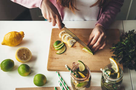 Upper view photo of a caucasian woman slicing fruits and making a mojito drink from lemon and limeの写真素材