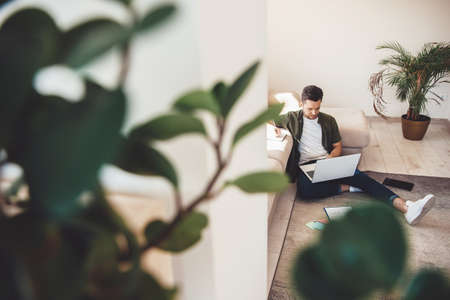 Front view photo with free space of a caucasian man working on the floor with a laptop and documentsの写真素材