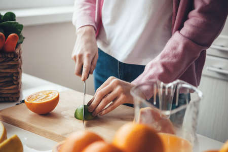 Close up photo of a caucasian woman with red hair and freckles slicing a lime and orange while...