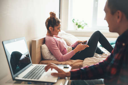 Side view photo of a caucasian couple working together at the laptop and smile using a phoneの写真素材