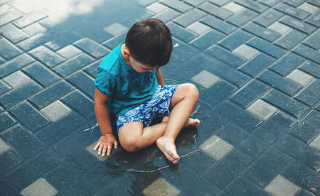 Upper view photo of a caucasian boy sitting in water outside during summer holidaysの写真素材