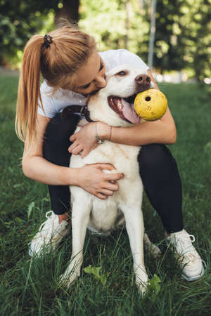 Close up photo of a blonde girl and her golden retriever playing with a ball on the grassの写真素材