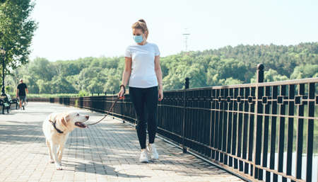 Charming lady with medical mask on face and blonde hair waking near the lake with a golden retrieverの写真素材