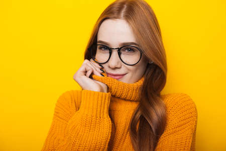 Close up photo of a caucasian woman with read hair and freckles wearing eyeglasses and orange sweater on a yellow backgroundの写真素材