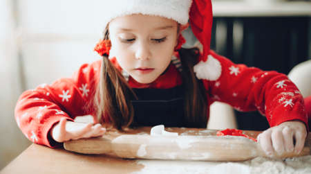 Lovely girl in christmas clothes preparing dough for holidays cookies at homeの写真素材