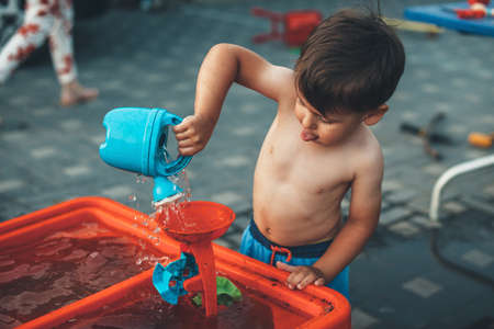 Cooling small caucasian boy playing with water and toys outside in his yard while his parents are working aroundの写真素材