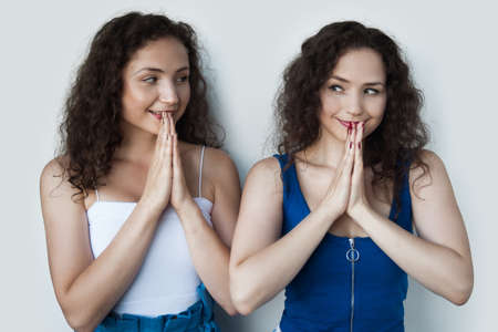 Caucasian twins are expecting something with pleasure gesturing with palms near mouth looking at...