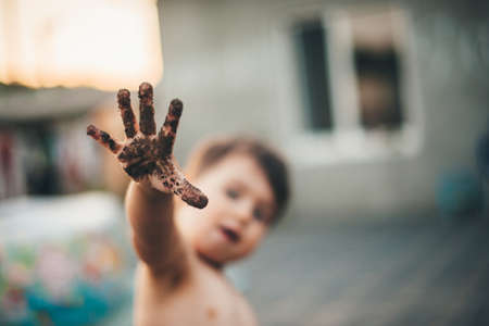 Caucasian undressed boy with dirty hand is playing outside in the ground having fun in a summer day